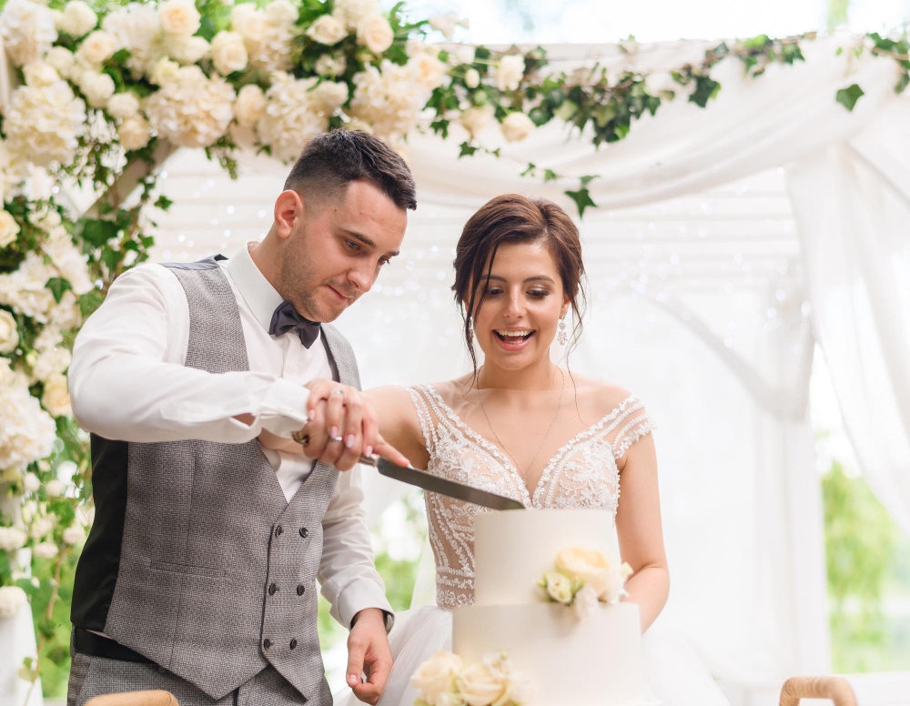 The bride and groom slice their wedding cake, marking a special moment in their celebration, assisted by a trusted wedding planner.