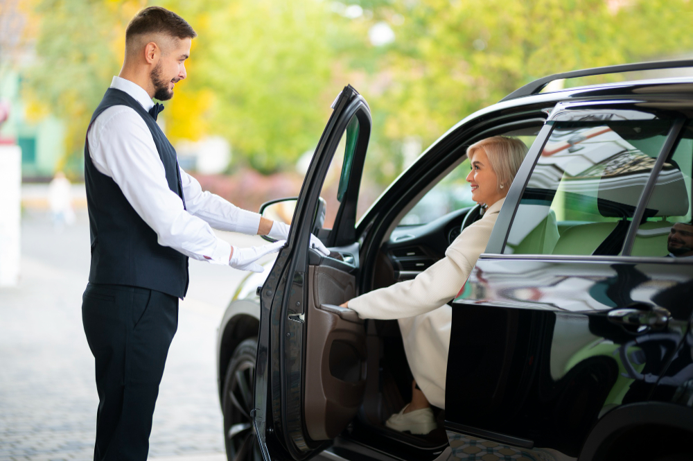 A man in a suit and tie is opening a black car door, highlighting the professionalism of corporate transportation services.