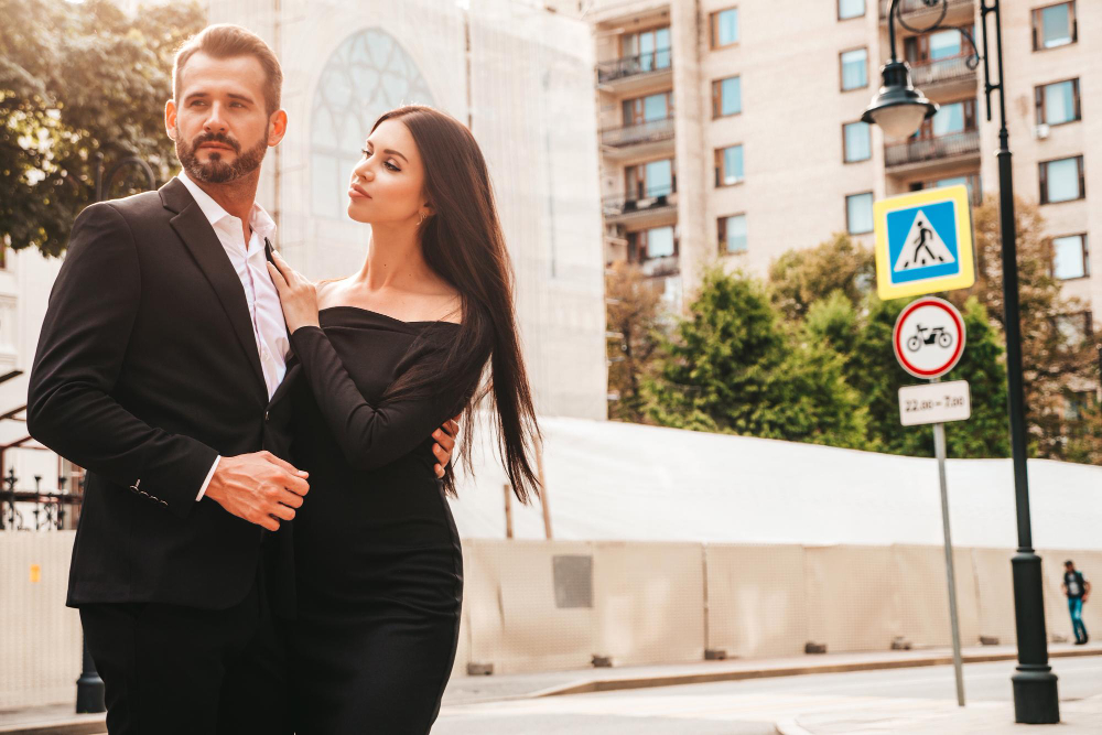 A stylish couple in formal wear stands on a vibrant city street, representing the glamour of Hollywood's elite escorts.